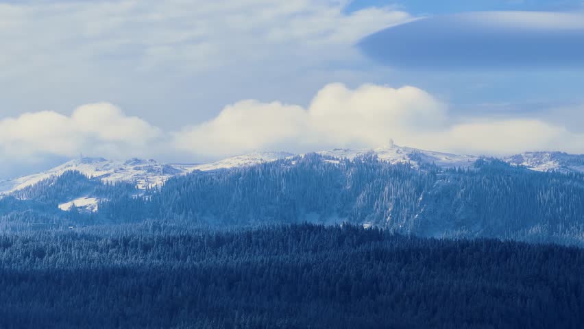 Bright light reveals tall mountain peaks covered in snow, standing above forested ridges and open sky