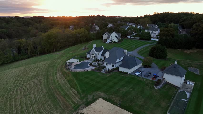 Modern american mansion with several buildings on hilltop of neighborhood. Colored forest trees during golden sunset time. Aerial orbit wide shot.