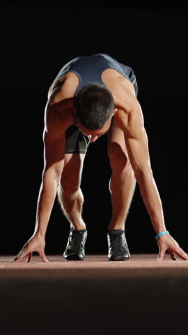 athlete man preparing to sprint start vertical slow motion fullhd studio dark background power discipline strength focus determination energy performance motivation fitness concept