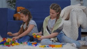 Sisters play with toy block on couch in living room while child and girl arrange building brick and toy part on rug near blanket and teddy bear showing sibling play and craft building activity at home - Powered by Shutterstock - Get 15% off with code: PIKWIZARD15