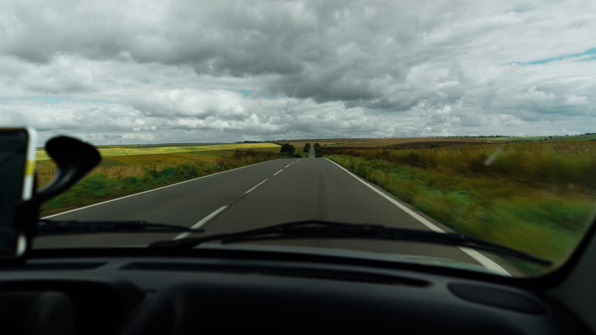View from a moving car passing endless sunflowers and crop fields under cloudy skies in Ukraine. A peaceful countryside scene showcasing rural life and vast agricultural land.