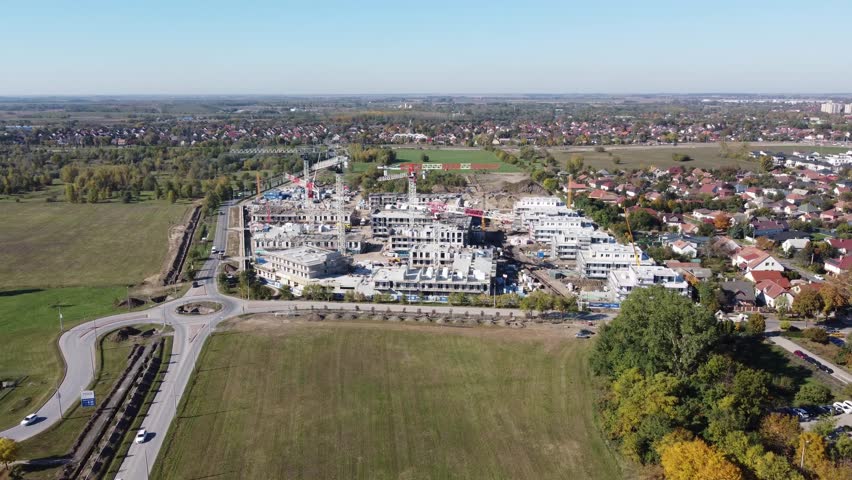 Aerial view of a large modern residential construction site featuring cranes, unfinished buildings, and active development in an urban suburban area. Construction machinery, materials, cranes.