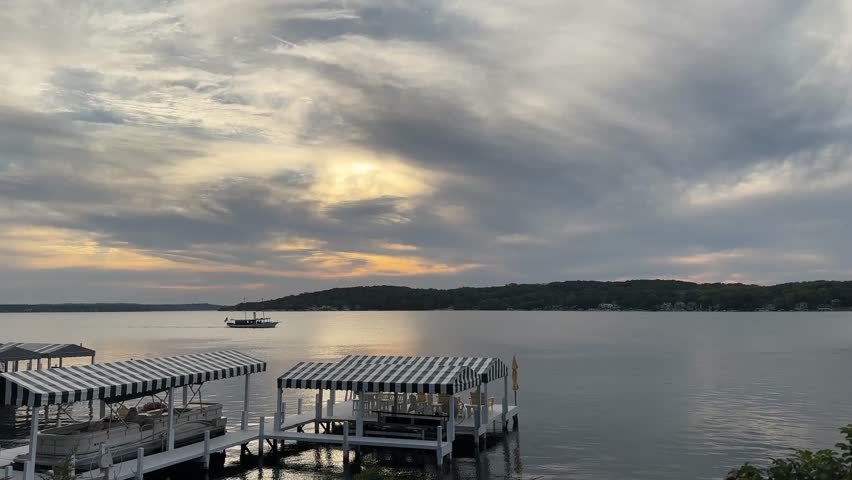 Boat Sailing Across Geneva Lake In Wisconsin On Peaceful Evening With Striped Dock Canopies In Foreground. wide shot
