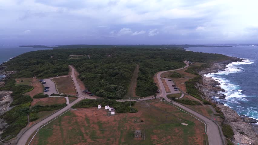 Aerial view of Conanicut Island and Beavertail Lighthouse in Beavertail State Park at the entrance to Narragansett Bay. The camera dolly out over the tip of the island and lighthouse on a cloudy day.