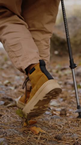 Pair of purposeful travelers in waterproof footwear with nordic walking poles moving towards water in pleasant autumn scenery. Crop of couple enjoying common outdoor activity while having day off.