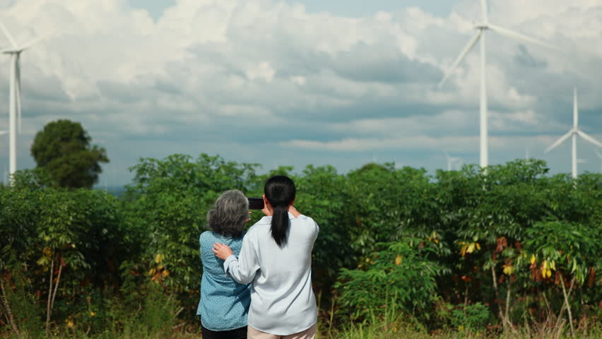 Two Asian female taking photo by smartphone. wind turbines in the background Representing Renewable Energy Eco Lifestyle and Sustainable Future. - Powered by Shutterstock - Get 15% off with code: PIKWIZARD15