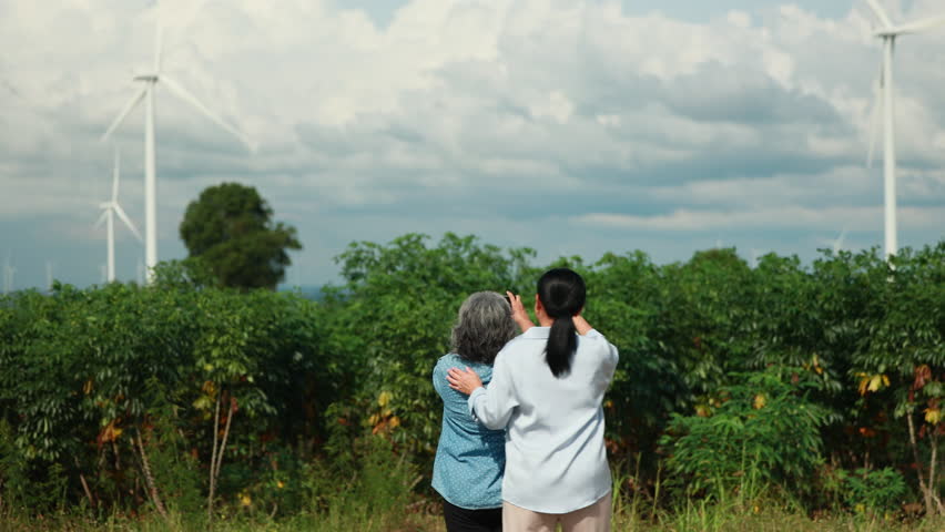 Two Asian female taking photo by smartphone. wind turbines in the background Representing Renewable Energy Eco Lifestyle and Sustainable Future. - Powered by Shutterstock - Get 15% off with code: PIKWIZARD15