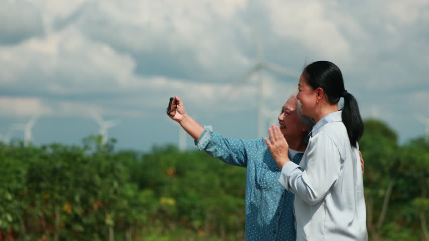 Two Asian female taking photo by smartphone. wind turbines in the background Representing Renewable Energy Eco Lifestyle and Sustainable Future. - Powered by Shutterstock - Get 15% off with code: PIKWIZARD15