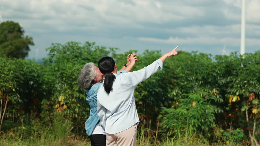 Two Asian female taking photo by smartphone. wind turbines in the background Representing Renewable Energy Eco Lifestyle and Sustainable Future. - Powered by Shutterstock - Get 15% off with code: PIKWIZARD15