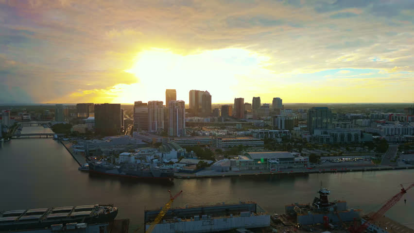 A brilliant aerial view of the bright sunset over the Ybor basin waterway with the Tampa skyline illuminated and shipping docks directly below.