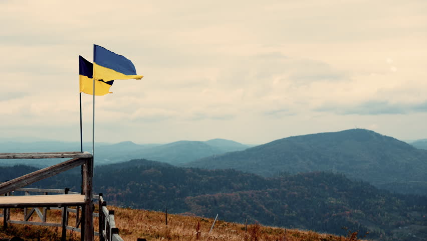 Ukrainian flag fluttering proudly on a mountain top overlooking the vast Carpathian ranges, epic landscape