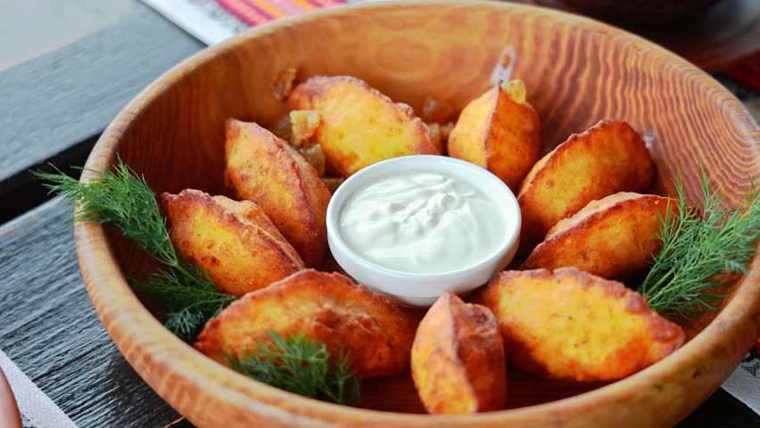 Golden roasted potato wedges served with sour cream and fresh dill in a rustic wooden bowl, delicious meal