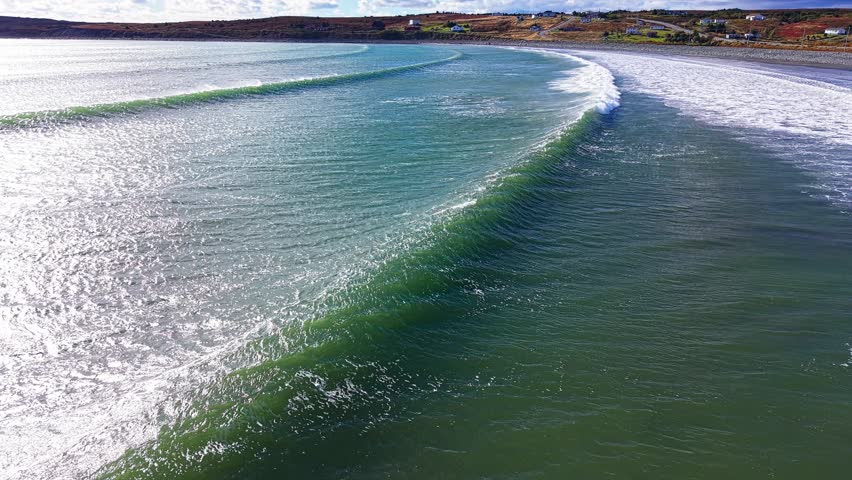 An aerial drone shot over Biscay Bay captures waves cresting across a sweeping sandbank and shallow channels, forming patterns of white surf against emerald water and swirling currents.