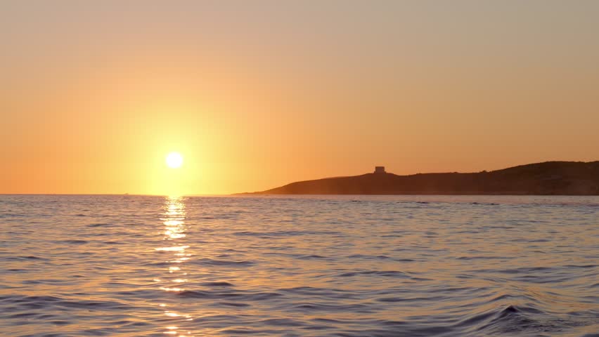 Serene sunset over calm Mediterranean sea with golden reflections and island silhouette on the horizon. Peaceful coastal evening scene.