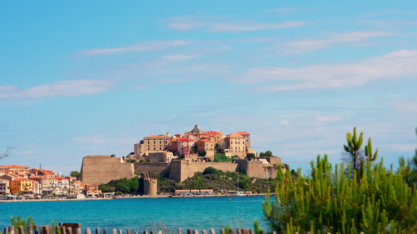Static shot of the historic town of Calvi in Corsica, France. View of the bastion Citadel overlooking the town. Calm turquoise sea. Summer holidays destination. Mediterranean island.