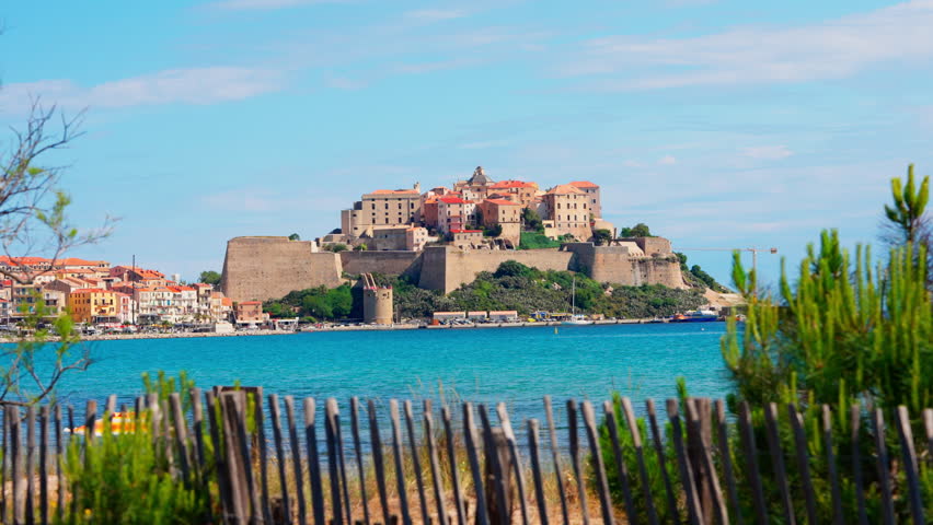 Static shot of the historic town of Calvi in Corsica, France. View of the bastion Citadel overlooking the town. Calm turquoise sea. Summer holidays destination. Mediterranean island.