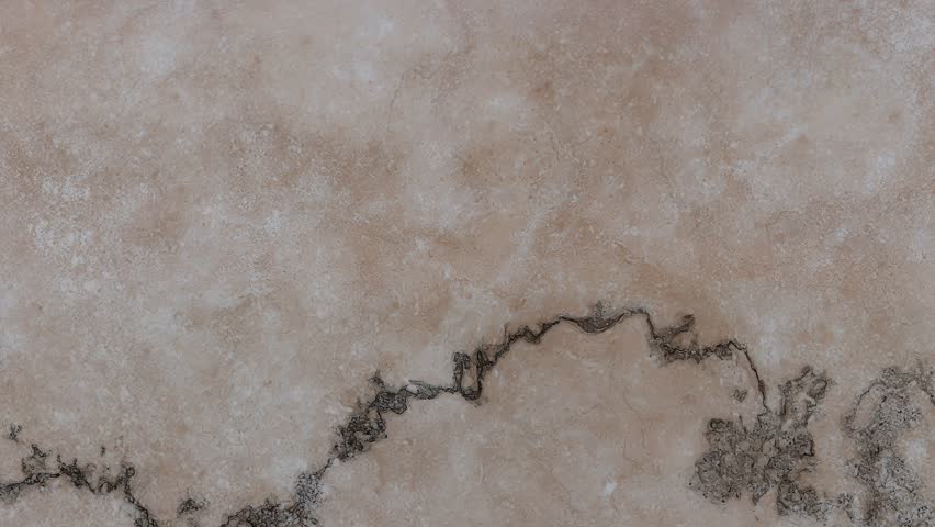 A light brown surface with a cracked texture and dark, jagged veins, exhibiting a mottled and weathered appearance.