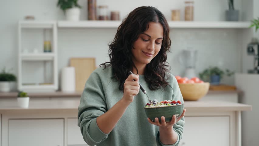 Video of young woman eating a healthy fruit bowl in the kitchen at home