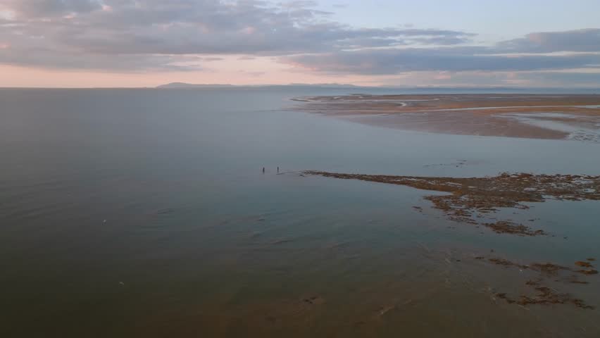 Two Lone Fishermen Standing On The Tide Line Of The Irish Sea At Low Tide At Sunset. Fleetwood, Lancashire, UK.