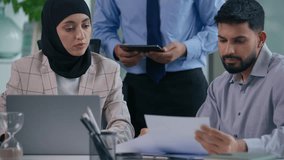 Arabian colleagues Muslim co-workers Hindu business team three Indian partners managers businesspeople in office working together teamwork collaboration discuss data with computer paper digital tablet - Powered by Shutterstock - Get 15% off with code: PIKWIZARD15