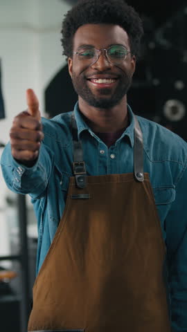 African American man working in roasted coffee fabric showing thumb up good job success recommend caffeine quality smiling looking camera technologist near roasting machine male roaster guy industry