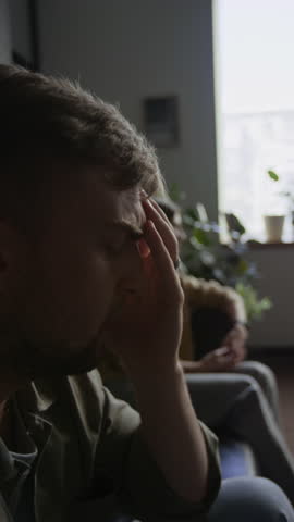 Vertical side view shot of couple in therapy session with focus on troubled young man speaking in foreground
