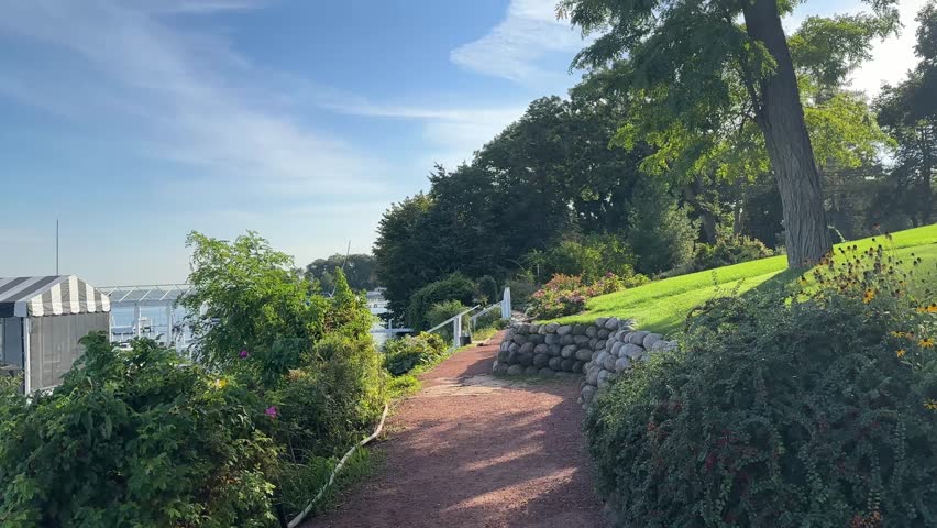 Lakeside Path On Shore Of Lake Geneva In Wisconsin, USA, Bordered By Flowers And Stone Walls On Sunny Day. POV shot