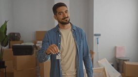 Young man holding house keys smiling in a new home interior surrounded by boxes indicating moving in progress. - Powered by Shutterstock - Get 15% off with code: PIKWIZARD15