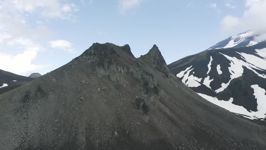 Aerial view of Lassen Peak in Northern California, USA, showcasing rugged volcanic slopes, rocky ridges, and patches of snow under a bright blue sky — a striking scene of natural geological beauty.