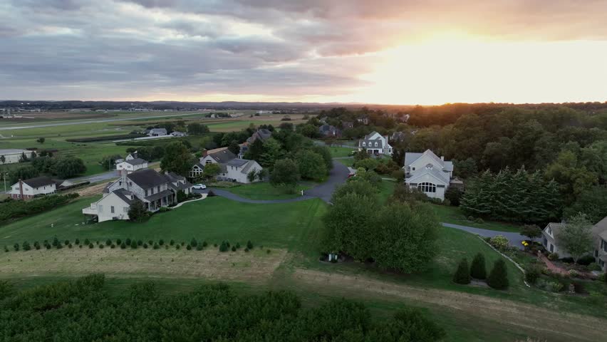 Aerial orbit shot of rural suburb neighborhood with solar panels on roof of homes. Idyllic green landscape with farm fields and green yards. Sunset time in Virginia, USA.