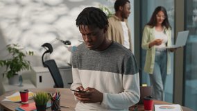 African American gadget addict business man male guy businessman chatting with mobile phone scrolling smartphone social media near two multiethnic office informal team coworkers with laptop walking - Powered by Shutterstock - Get 15% off with code: PIKWIZARD15