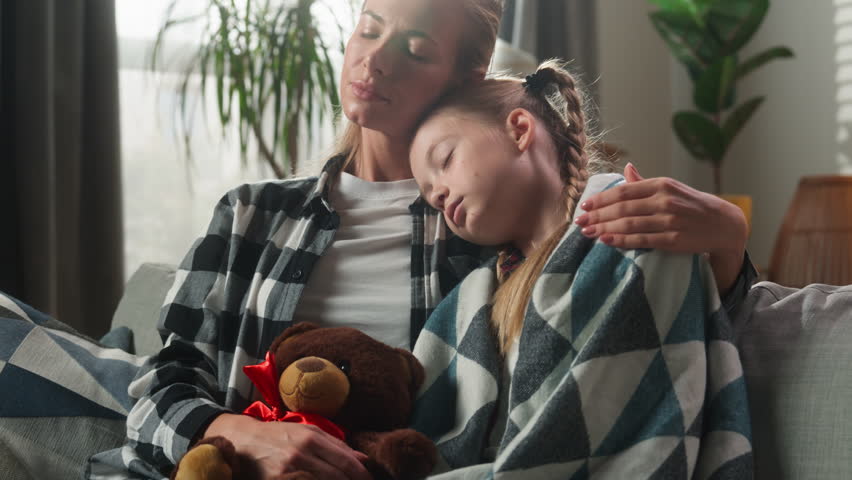Caucasian family cuddling at home caring mother comforting sick daughter coughing ill wrapped in blanket on couch sad kid child girl hugging Teddy Bear cough sick love support medicine health problem