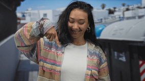 Young hispanic woman points both fingers down at a recycling bin on street while smiling broadly; playful confidence. - Powered by Shutterstock - Get 15% off with code: PIKWIZARD15