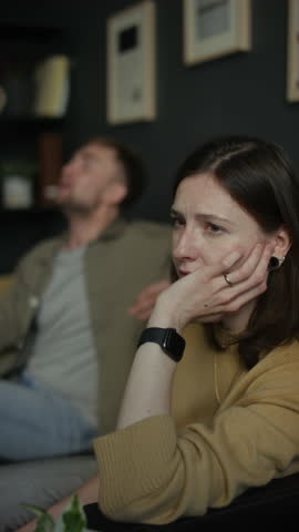Vertical shot of couple arguing in therapy session with focus on troubled young woman looking away in foreground