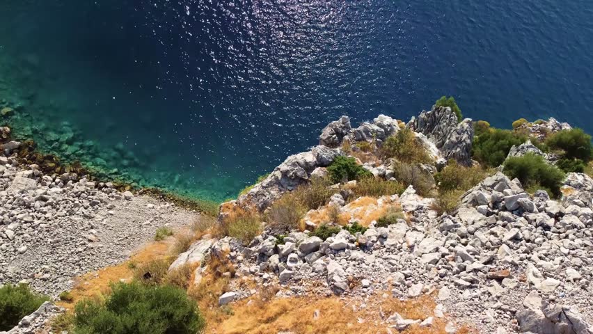 aerial drone shot captures the pristine beauty of Cennet Koyu Paradise Bay in Turkey, showcasing its vibrant turquoise waters, rugged rocky coastline, and lush Mediterranean vegetation under clear blu