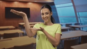 Young hispanic woman smiling and presenting palms up in a classroom building, palms cupping an invisible object; confidence. - Powered by Shutterstock - Get 15% off with code: PIKWIZARD15