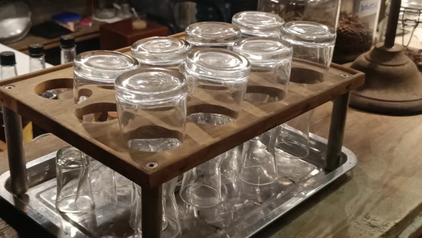 An aesthetic close-up captures a wooden rack filled with glasses, illustrating a focus on beverage service and refined presentation within a cafe or