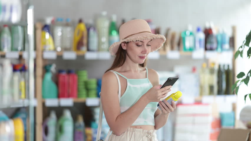Woman in a straw hat is preparing for the summer summer season, she scans on phone a mosquito and insect barcode repellent on her phone and reads the composition. High quality 4k footage
