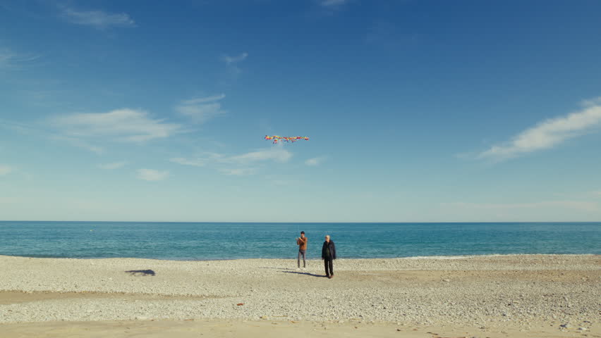 Father and son playing with kite near the ocean on the beach for the day