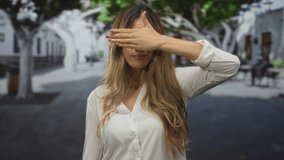 Young blonde woman covers face with hand in plaza; shyness secrecy. - Powered by Shutterstock - Get 15% off with code: PIKWIZARD15
