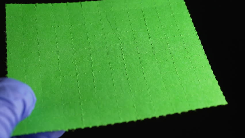 Hands of the drug dealer in gloves break or tear the LSD strip blotters with dry drops of Lysergic acid drug lucy or Ellis D. Hallucinogenic drug for sale in clubs, parties and street.