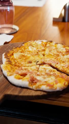 Cinematic close-up parallax shot glides over a delicious freshly baked pizza, sliced and served on a rustic wooden board in a restaurant