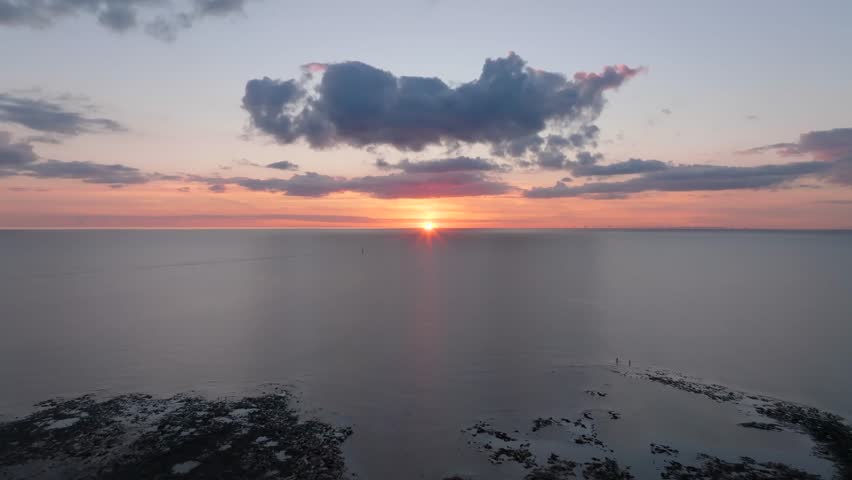 Two Lone Figures On Tide Line At Sunset With Camera Flight Over Calm Irish Sea Towards Setting Sun. Golden Hour. Fleetwood, Lancashire, UK.