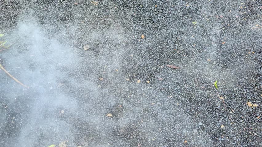 Dense white smoke or fog drifts across outdoor gravel ground, natural daylight, static overhead shot