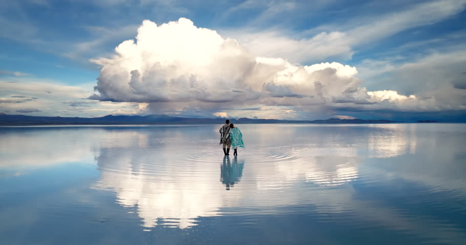 Tourist couple with traditional Bolivian garments reflected in Uyuni salt flat