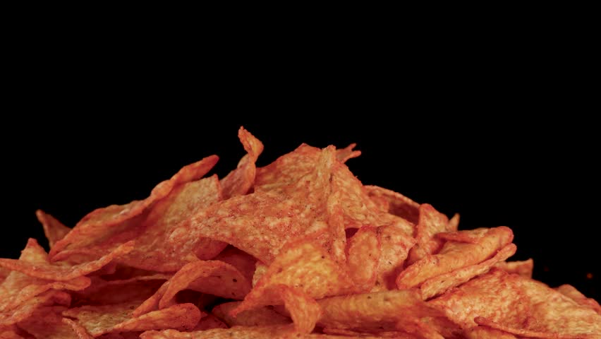 Human hand selects and lifts tortilla chip from vibrant nacho pile, studio lighting, static camera