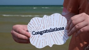 Young White Woman Holds Up Handmade Card That Says Congrats on the Beach at the Lake 4K Video Stock Footage - Powered by Shutterstock - Get 15% off with code: PIKWIZARD15