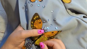 Female hands with pink nails carefully sewing an orange butterfly applique on cloth, demonstrating patience and artistic skill. Hand painted butterfly and beads handiwork - Powered by Shutterstock - Get 15% off with code: PIKWIZARD15