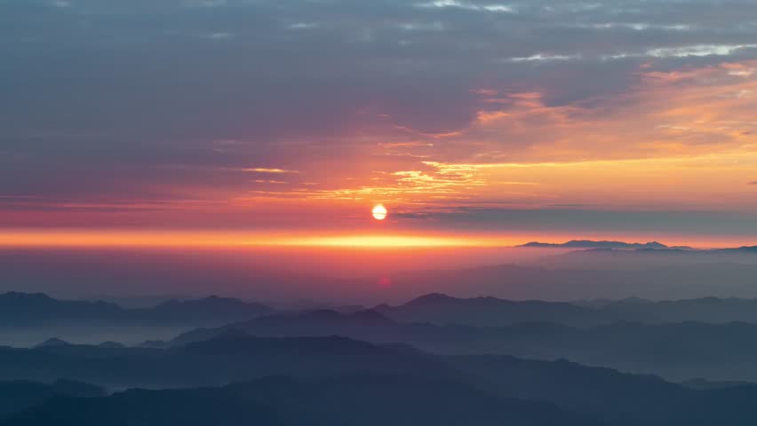 Epic Horizon: Fiery Sun Setting Over Layered Mountain Ridges