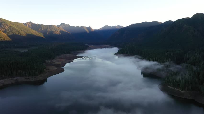 4K aerial drone footage of sunrise at Wynoochee Lake dam in Olympic National Forest, Washington State, USA, showing calm water, low clouds, and forested mountain landscape in peaceful morning 